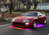 A red car with underglow LED lights in multiple colors, driving on a residential street at dusk.